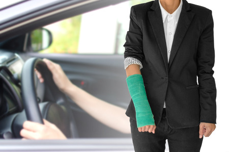 insurance concept, injured businesswoman with green cast on hand and arm  and wearing black suit standing isolated on blurred background woman hand driving car.の写真素材