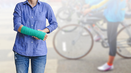 Female patient wearing blue shirt with green cast on arm isolated on blurred background woman riding a bicycle, body injury concept.の写真素材
