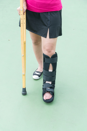 Injured woman wearing sportswear  painful leg with black cast and wooden crutches on basketball courtの写真素材