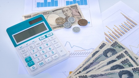 Calculator with Japanese currency yen bank notes and coin on finance chart and graph background, finance planning concept.の写真素材