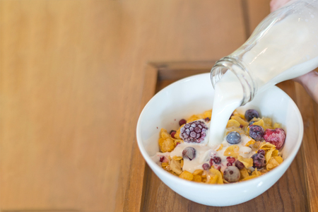 fresh milk on the white cup, cornflakes cereal, strawberry, blackberry and milk in a white bowl,...