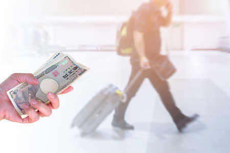 hand woman with Japanese currency yen bank notes on blurred background travelers walking with a luggage at airport terminal, travel costの写真素材