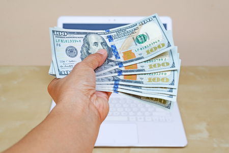 business woman hand holding American dollar currency on white laptop on wood desk.の写真素材