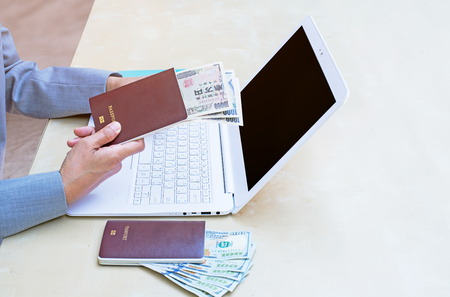 business woman holding passport, American dollar currency  and using modern laptop on wood desk.の写真素材