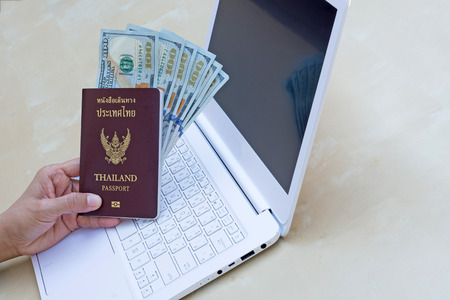 business woman holding passport, American dollar currency  and using modern laptop on wood desk.の写真素材