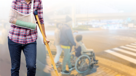 broken arm, injury woman standing wearing shirt and jeans with arm cast and holding wooden crutches...
