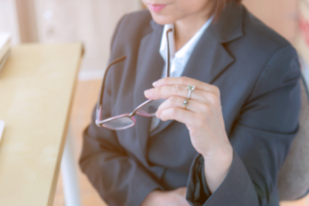 blurred background business woman sitting and holding eyeglasses working on desk in office.の写真素材