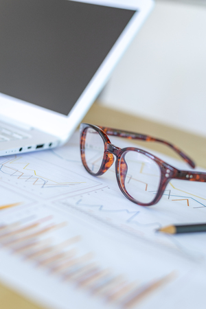 desk workplace, eyeglasses, pencil and laptop on report graph on wood  desk, business concept.の写真素材