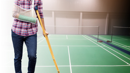 Injured woman with green cast on hand and arm on background badminton indoor court, sport accident pain concept.の写真素材