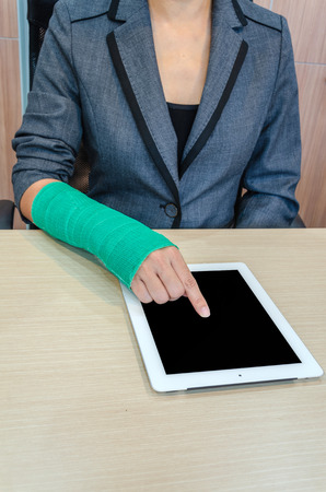 woman with broken hand and green cast  working on tablet computer in officeの写真素材
