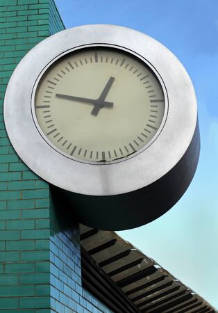 Public clock hanging from green facade buildingの写真素材