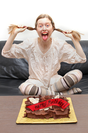 Happy teenager celebrating sweet sixteen birthday with chocolate cake laughing and pulling her pigtailsの写真素材