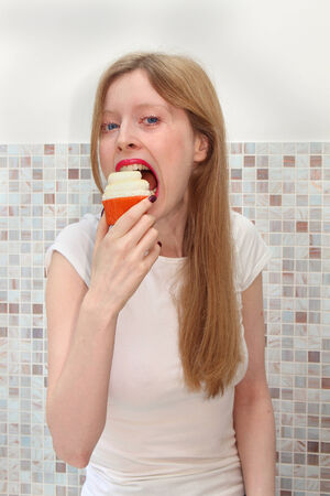 Young blonde girl eating tasty cupcake dessertの写真素材