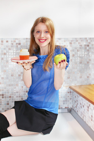 Young beautiful girl holding cupcake and apple in her handsの写真素材