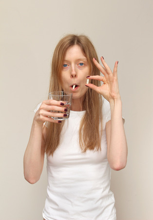 Young pale girl taking prescription medicine pills with glass of waterの写真素材