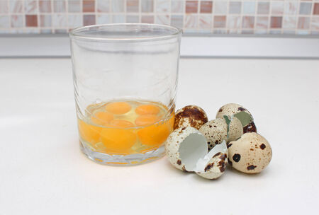 Broken quail eggs in transparent glass with empty shells next to itの写真素材