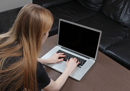 Young teenage girl from back typing on laptop keyboard with empty screen which can be used for inserting your contentの写真素材