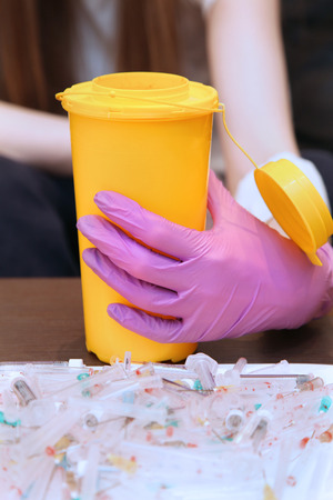 Female hand holding yellow waste container with used syringes and needles in frontの写真素材