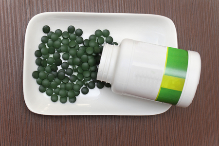 Spirulina superfood tablets from plastic bottle on white plateの写真素材