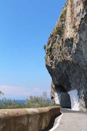 Small tunnel through mountain on narrow road next to coastlineの写真素材