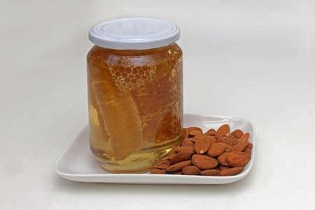 Comb honey in glass jar with raw almondsの写真素材