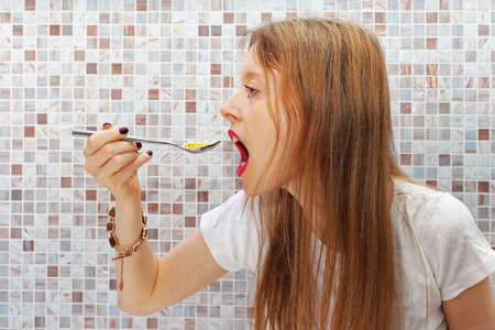 Young woman addict eating pills with a spoonの写真素材