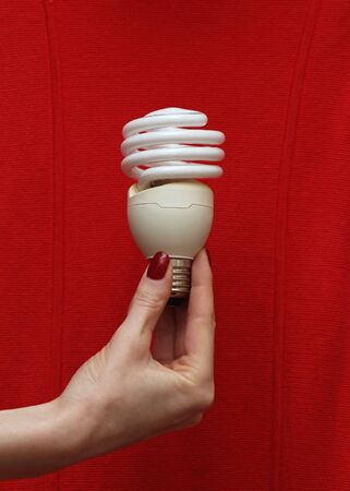 Female hand holding energy saving lightbulb on red backgroundの写真素材