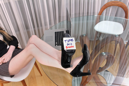 Young women with long legs on office desk and time for break signの写真素材