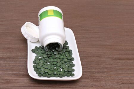 Spirulina super food tablets flowing out of plastic containerの写真素材