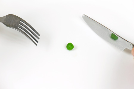 Green pea on white plate with fork and knifeの写真素材