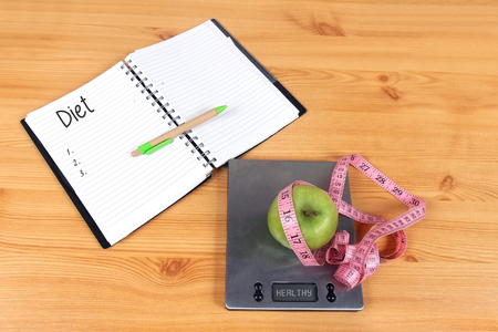Open diet plan notebook and scale with green apple and tape measureの写真素材