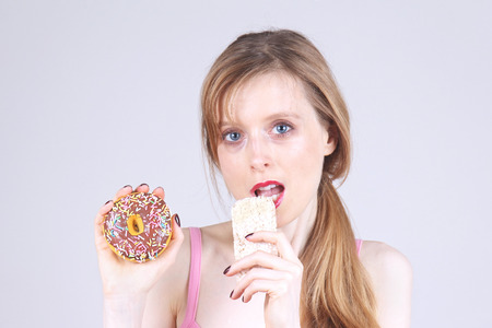 Young woman making food choices eating rice cake and holding donutの写真素材