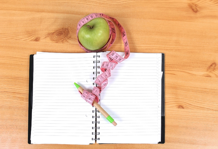 Open notebook with apple and tape measure around penの写真素材