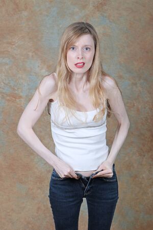 Young slim girl struggling to zip up tight skinny jeans showing frustration on her faceの写真素材
