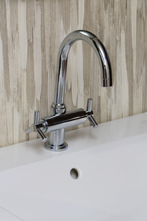 Modern silver tap over ceramic washbasin and beige tiles behindの写真素材