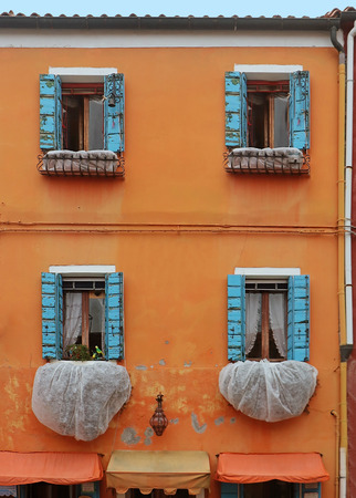 Open retro faded windows with wooden blinds on orange facade houseの写真素材