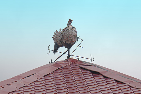 Rooster weather vane figurine on top of the roof with blue sky in the backgroundの写真素材