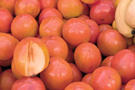 Large pile of persimmon fruit originally cultivated in Asia sold on European marketの写真素材
