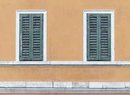 Two retro closed windows with wooden shades on yellow facadeの写真素材