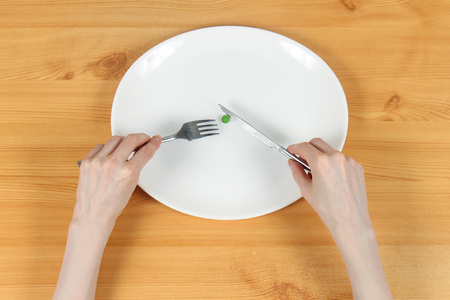 Skinny female hands toying with single pea in white plate as eating disorder conceptの写真素材