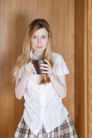 Young woman holding tea cup in the corner of the roomの写真素材