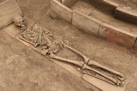 Human skeleton next to an open tomb on dirty sandの写真素材