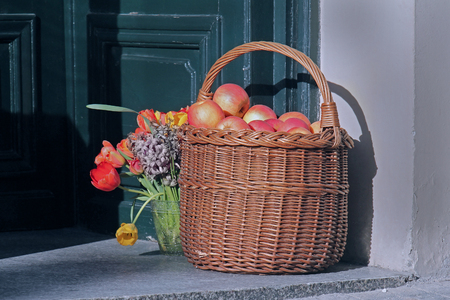 Rattan basket full of red apples standing in front of entrance doorの写真素材