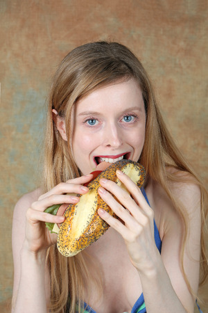 Young blue eyed woman smiling while eating a sandwichの写真素材