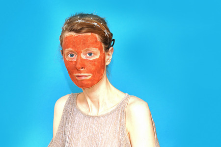Young woman with clay mask on her face with blue backgroundの写真素材