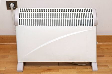 Electric heater on wooden floor inside interior and plugged into socket on a wallの写真素材