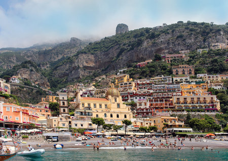 Positano, Italy - June 28, 2014; People on famous Spiaggia Grande Positano beach swimming in the sea and tanning under the sun on luxury Italian resort with colorful houses in the background.のeditorial素材