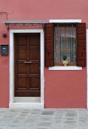 Closed wooden brown door on retro house entrance with open window and pink facadeの写真素材