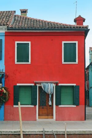 Small retro residential house with red facade and green closed windowsの写真素材