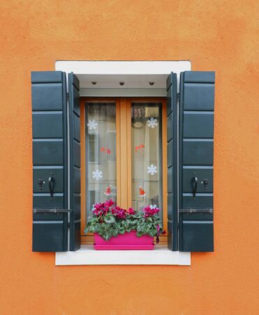 Retro window with open wooden shades on orange wall facadeの写真素材